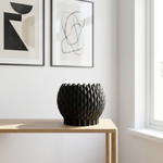 Black textured vase on a wooden table with abstract art in the background