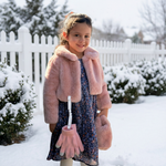 Young girl in a pink coat and gloves standing in the snow.
