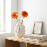 White textured vase with orange flowers on a wooden table next to books and a framed picture.
