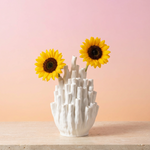 White textured coral vase with two sunflowers on a pale slab against a pink and peach background