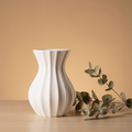 White textured vase on a wooden surface with a branch of eucalyptus against a beige background