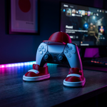 Gaming controller with red and white shoes on a desk in front of a computer screen.