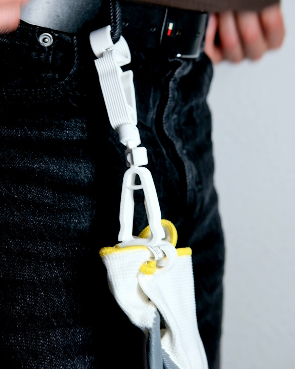 White safety hook with yellow accents attached to a black strap, worn on a person's waist.