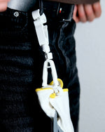 White safety hook with yellow accents attached to a black strap, worn on a person's waist.