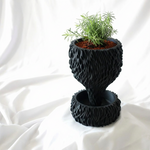 Black textured planter with a small plant on a white fabric background