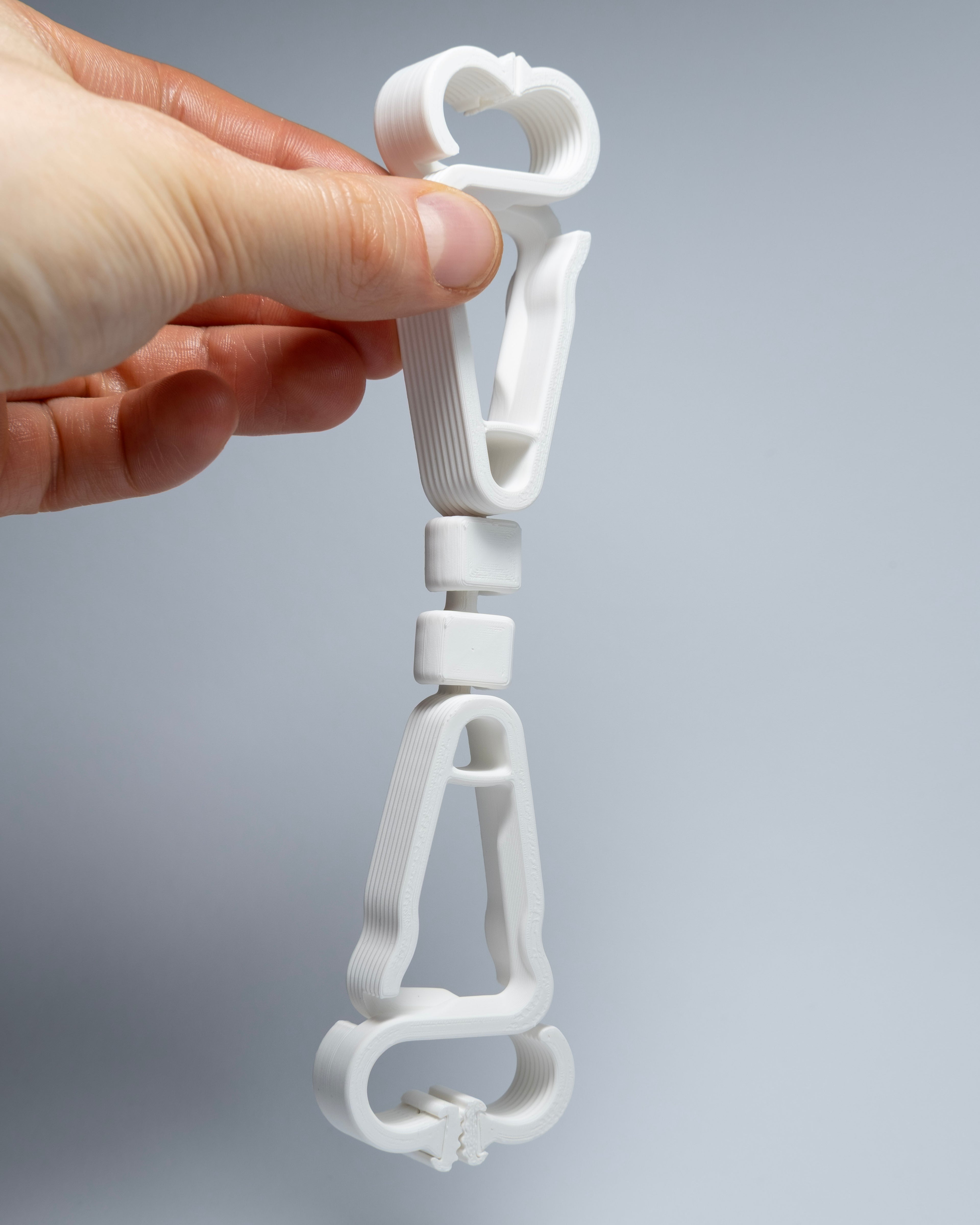 Hand holding a white plastic clip against a gray background