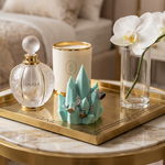 Decorative items including a Lalique perfume bottle, candle, jewelry stand with rings, and a vase with an orchid on a marble surface.