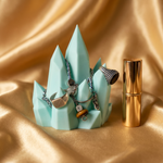 Jewelry set on a turquoise stand with a gold lipstick on a gold fabric background