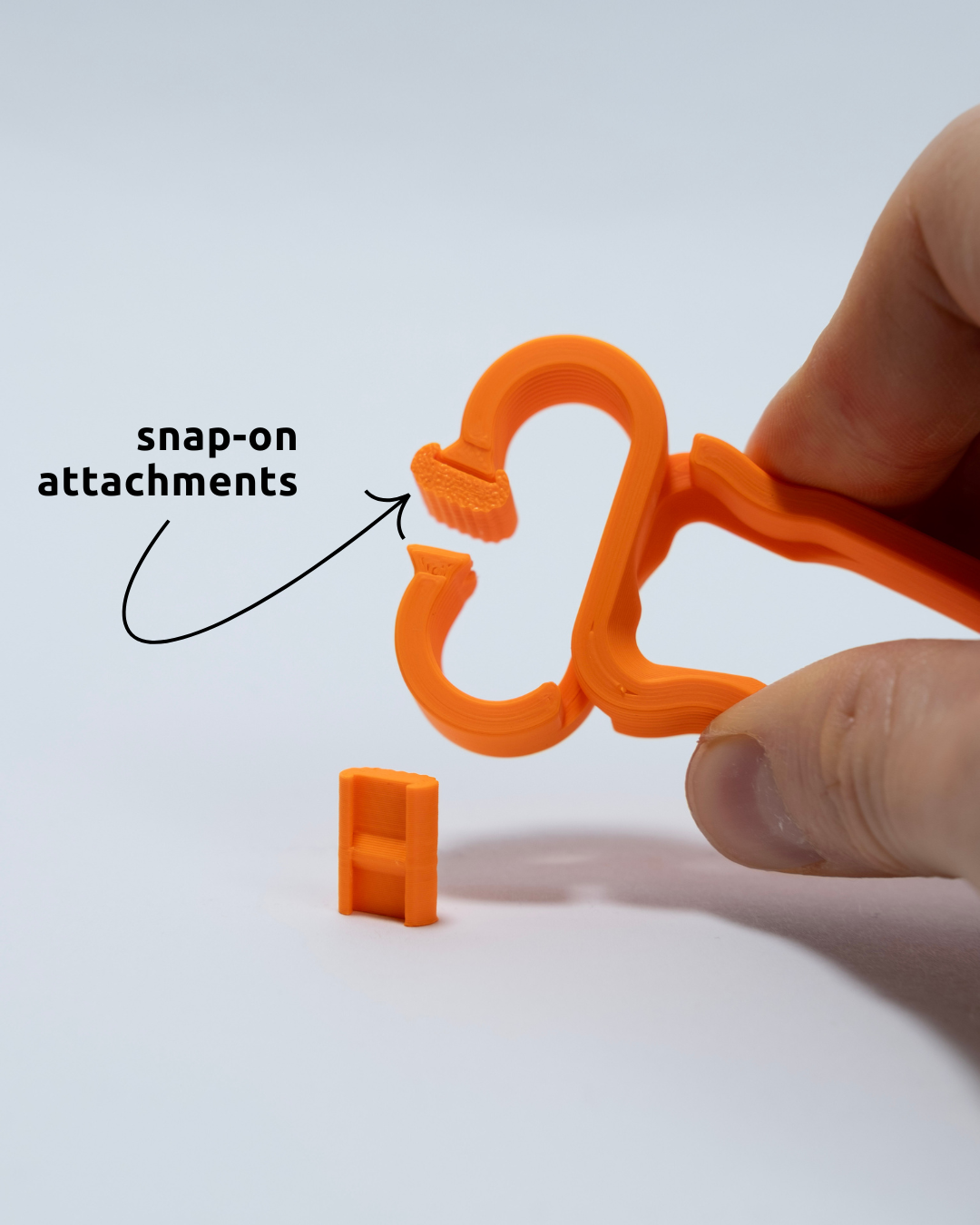 Hand holding an orange 3D-printed object with a smaller component labeled 'snap-on attachments' on a white background.