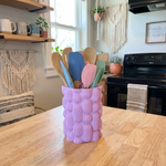 Purple textured utensil holder with colorful spatulas on a kitchen counter