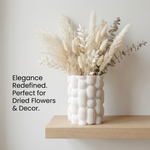 White textured vase with dried flowers on a wooden shelf against a light background