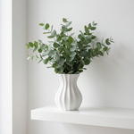 White vase with green leaves on a white surface against a white background
