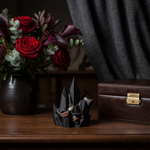 Black crystal-shaped jewelry holder with rings, chains and a watch beside red roses and a wooden box
