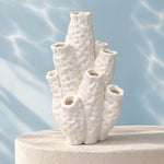 White coral-shaped vase with bumpy tubular branches on a round pedestal against a blue rippled-light background