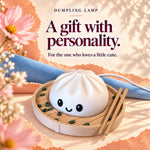 Dumpling lamp ad reading 'A gift with personality': a smiling white dim sum night light in a steamer basket with chopsticks on peach paper and blue cloth, a cute foodie gift.