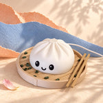 White dumpling lamp, a kawaii decor night light with a smiling face, in a steamer basket with chopsticks on a blue cloth with soft leaf shadows and a white power cord.