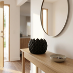 Black decorative vase on a wooden console table with a round mirror above.