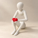 White Love’s Embrace figure holding a red heart against a neutral ivory background