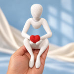 White Love’s Embrace figure holding a red heart, shown resting in a hand against a blue background