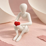 White Love’s Embrace figure holding a red heart on pink paper with curved ivory paper shapes