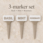Three white and beige plant markers labeled Basil, Mint and Rosemary