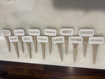 Twelve white and beige plant markers arranged in two rows on a stone surface