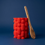 Red textured container with a wooden spoon on a blue background