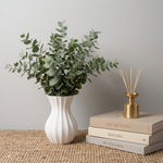 White vase with greenery, gold diffuser, and books on a textured surface