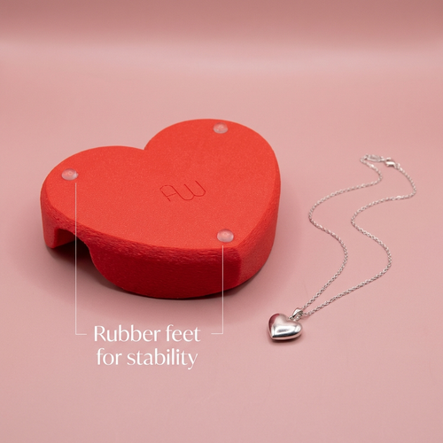 Red heart-shaped object with 'AU' branding and a silver necklace on a pink background