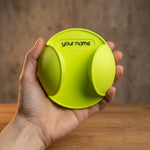 Hand holding a lime-green round racket mount with two curved grips and the sample text "your name".