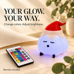 Elf hat garlic lamp glowing soft lavender-blue on cream cloth beside a color remote and green leaves, with on-image text about adjustable colors and brightness. A color-changing garlic lamp for holiday decor.