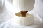 Close-up of the tan wavy core connecting the white ribbed pot and open reservoir bowl