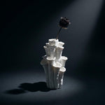 White coral-shaped vase holding one dark flower under a spotlight against a black background