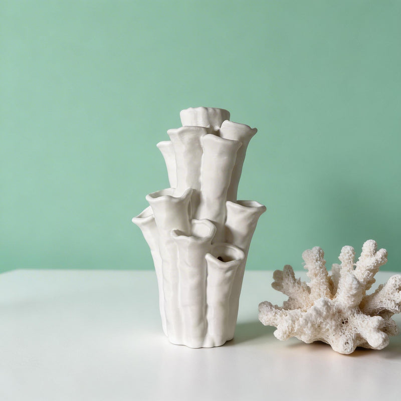 Empty white coral-shaped vase with flared openings beside a piece of coral on a pale tabletop