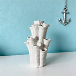 Empty white coral-shaped vase with flared openings on a white surface beneath a hanging anchor decoration
