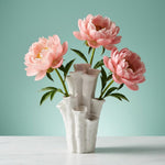 White coral-shaped vase with flared openings and three pink flowers against a mint background