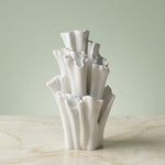 Empty white coral-shaped vase with tall ruffled tubes on a veined tabletop against a pale green background