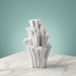 Empty white coral-shaped vase with tall ruffled tubes on a veined tabletop against a teal background