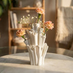 White coral-shaped vase with peach and tiny white flowers on a sunlit table in front of a bookshelf