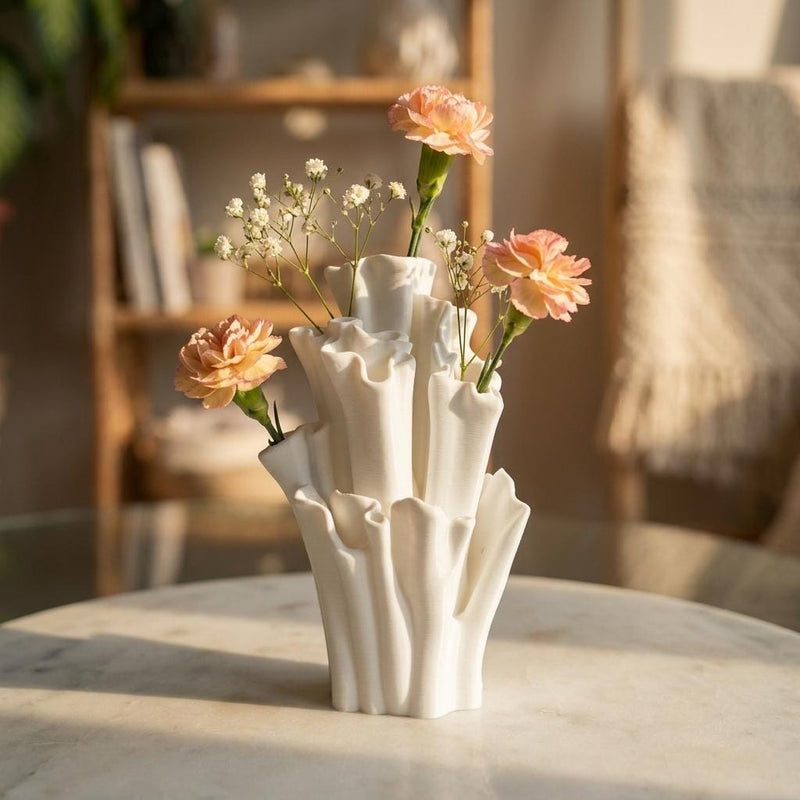 White coral-shaped vase with peach and tiny white flowers on a sunlit table in front of a bookshelf