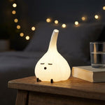Glowing garlic lamp on a dark bedside table beside a glass and string lights
