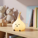 Yellow glowing garlic lamp on a shelf with books and stuffed bears