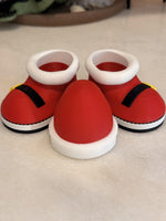 Santa controller stand set with two red Santa boots with white cuffs, black straps and yellow buckles and a red Santa hat with white band, a stocking stuffer controller holder, shown without a controller.