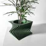 Angled view of a green ribbed square planter holding a leafy plant on a white table.