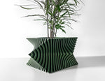 Front view of a green planter with twisting vertical ribs and a leafy plant against a white wall.