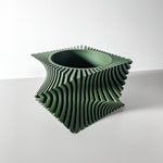 Empty green square planter with twisting vertical ribs and a round opening on a white table.